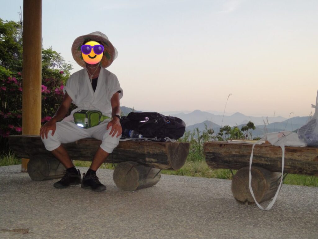 五色台の東屋で休憩する歩き遍路姿の私：背景には香川特有の幻想的な山々
